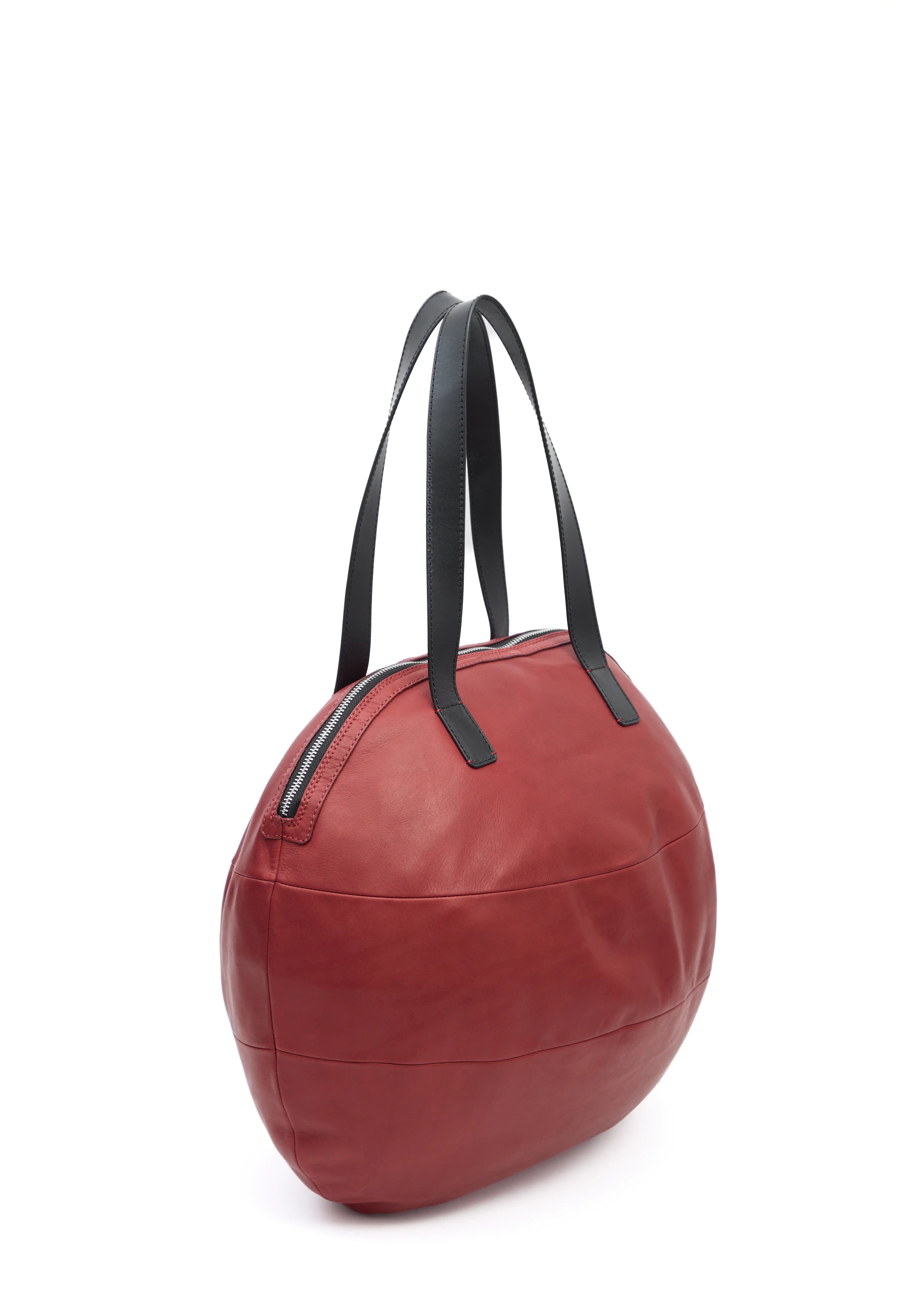 Side view of the Philini Nataly Handbag in bordeaux aniline calf leather, round silhouette with two black handles and bronze zipper. Unique red designer handbag